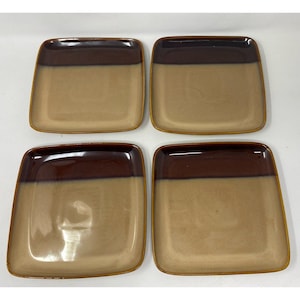 May include: A set of four square ceramic plates featuring a two-tone design with a dark brown glazed upper section and a lighter tan glazed lower section. Each plate has rounded corners and a smooth, glossy finish across the surface.