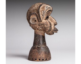 May include: A wooden sculpture of a human head with a stylized face and a carved neck. The sculpture is painted in shades of brown and black.