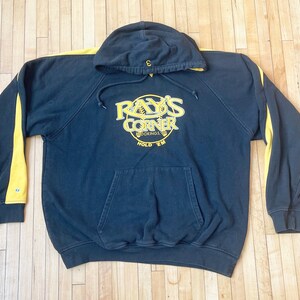 May include: Black hooded sweatshirt with yellow stripes on the sleeves. The front features a gold embroidered logo that says "Ray's Corner" with the words "Rookies" and "Hold 'Em" underneath.
