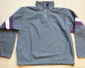 May include: A gray Champion fleece pullover with purple and white striped sleeves. The zipper has a pull tab with the Champion logo.