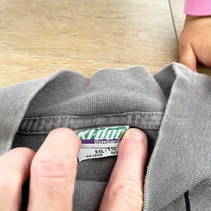 Może przedstawiać: Szara w paski koszulka z zielono-białą metką z napisem "XL/T1G Bombardir CA 28395 RN 9"