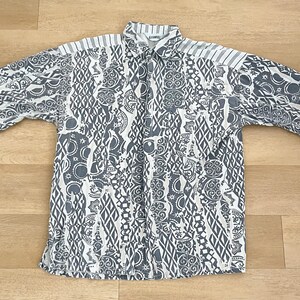 May include: A white button-down shirt with a black and white geometric pattern. The shirt has short sleeves and a collar.