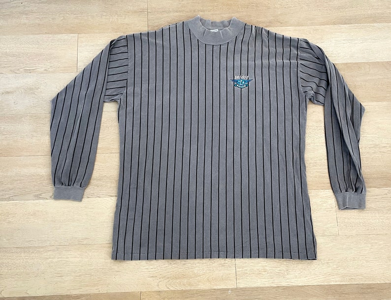 Może przedstawiać: Szara w paski koszula z długim rękawem z czarnym logo z napisem "Air City" i grafiką samolotu.