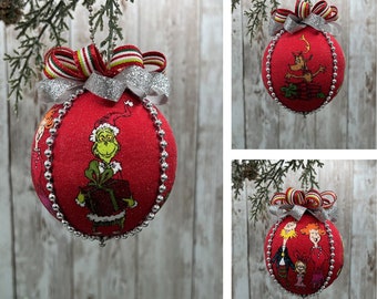 May include: Red Christmas ornaments with Dr. Seuss characters. Each ornament has a silver beaded trim and a decorative bow with silver, red, and green ribbons. The ornaments are hanging from a green branch.
