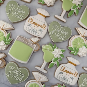 May include: A set of green and white decorated sugar cookies featuring a heart-shaped cookie with the text "Marilee & Matt", a bottle-shaped cookie with the text "Chappell Tequila 100% Agave", a margarita glass cookie, and a ring cookie with a lime slice.