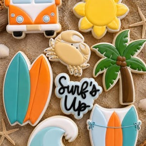 Könnte beinhalten: Eine Sammlung von Keksen zum Thema Strand, darunter eine gelbe Sonne, eine Krabbe, eine Palme, Surfbretter, eine Welle und ein Van. Die Kekse sind mit leuchtenden Farben und dem Schriftzug "Surf's Up" verziert. Die Kekse sind auf einer sandigen Oberfläche angeordnet.