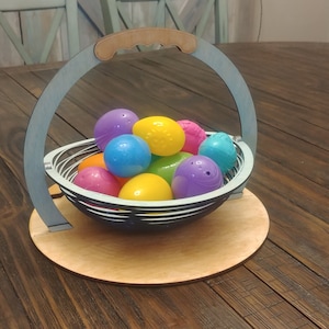May include: A blue wooden basket with a handle, filled with colorful plastic Easter eggs. The basket is sitting on a wooden table.