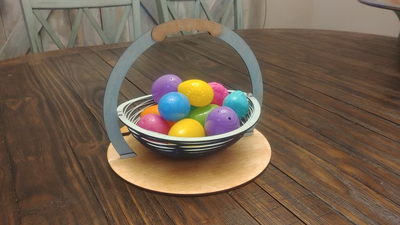 May include: A blue wooden basket with a handle, filled with colorful plastic Easter eggs. The basket is sitting on a wooden table.