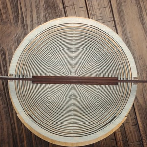 May include: A wooden bowl with a circular design made of concentric rings. The bowl is made of light wood and has a dark brown handle.
