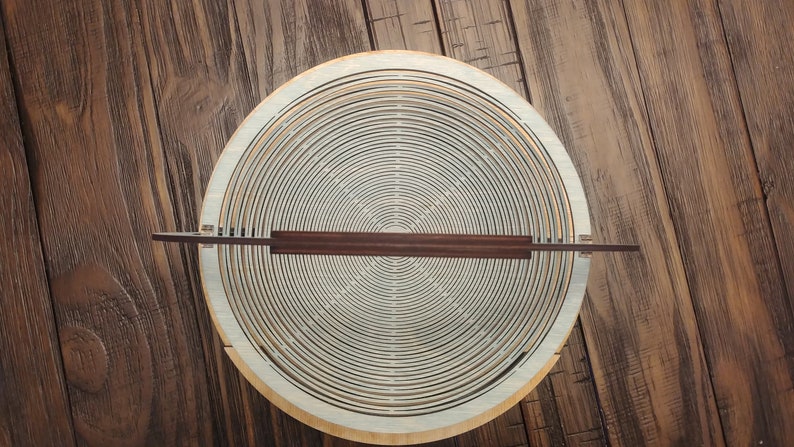 May include: A wooden bowl with a circular design made of concentric rings. The bowl is made of light wood and has a dark brown handle.