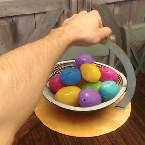 May include: A wooden basket with a handle, filled with colorful plastic Easter eggs. The basket is sitting on a wooden table.