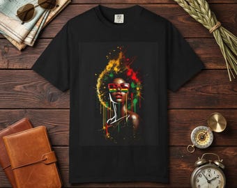May include: Black t-shirt with a colourful graphic of a woman wearing glasses and with vibrant hair. The artwork uses red, yellow, and green accents. The design is centered on the shirt, creating a bold visual statement.