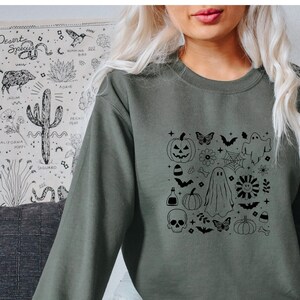Puede incluir: Una sudadera verde con un estampado gráfico negro de varios iconos de Halloween, incluyendo calabazas, fantasmas, murciélagos y arañas.
