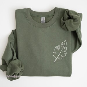 May include: A green sweatshirt with a white outline of a leaf on the left side of the chest.