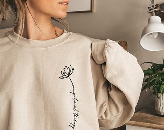 Puede incluir: Una sudadera beige con un gráfico de diente de león negro y el texto "terapia ocupacional" escrito verticalmente.