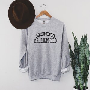 May include: Gray sweatshirt with the text "I'm just out here trusting God" in a retro font.
