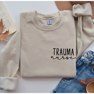 May include: A beige sweatshirt with the text "TRAUMA nurse" in black script on the front.