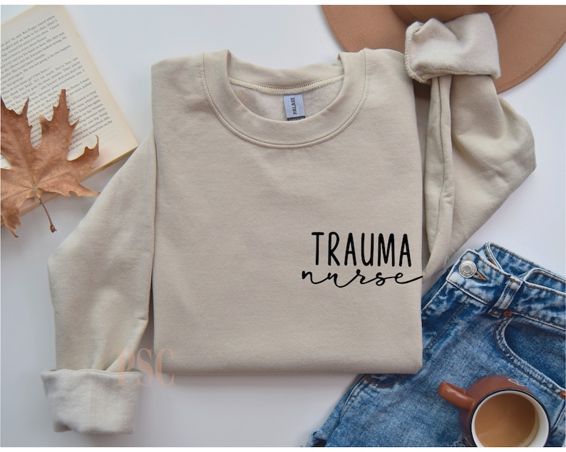 May include: A beige sweatshirt with the text "TRAUMA nurse" in black script on the front.