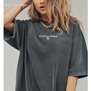 May include: Dark grey t-shirt with the text "greyhound mom" and a white greyhound silhouette. The shirt has short sleeves and a relaxed fit.