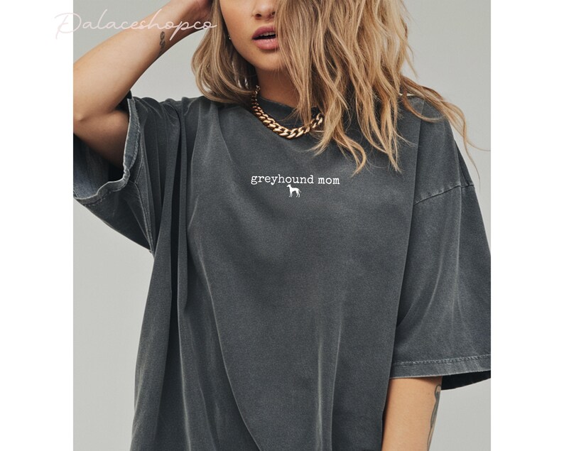 May include: Dark grey t-shirt with the text "greyhound mom" and a white greyhound silhouette. The shirt has short sleeves and a relaxed fit.