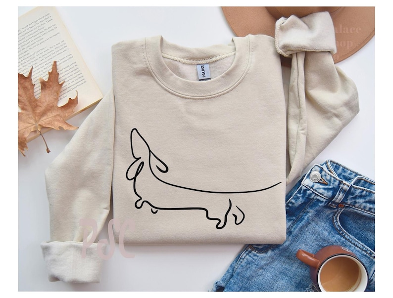 May include: A beige sweatshirt with a simple line drawing of a dachshund on the front.