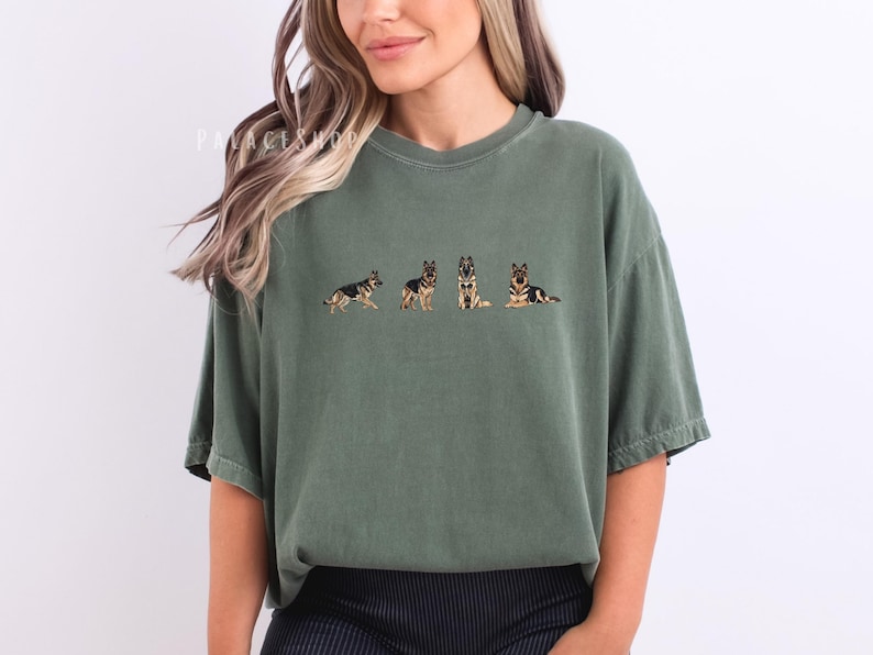 Op de afbeelding: Olijfgroen T-shirt met een geborduurd ontwerp van een Duitse herder in vier verschillende poses. Het shirt heeft een relaxte pasvorm en een ronde hals. De tekst "PALACEWOOD" is zichtbaar linksboven op het shirt.