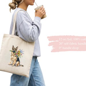 Peut inclure: Un sac fourre-tout en toile de couleur cr&egrave;me avec une illustration &agrave; l'aquarelle d'un berger allemand tenant des fleurs. Le sac a des anses de 50,8 cm et une hauteur de 22,86 cm. Fabriqu&eacute; en toile 100% coton.