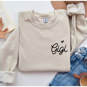 May include: A beige sweatshirt with the word "Gigi" written in black cursive with a small heart above it.