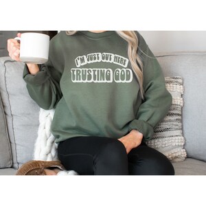 May include: A green sweatshirt with the text "I'm just out here trusting God" in white letters.