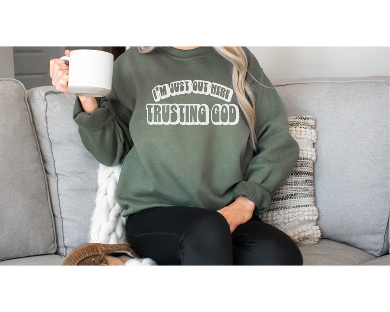 May include: A green sweatshirt with the text "I'm just out here trusting God" in white letters.
