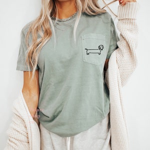 May include: A sage green t-shirt with a small black dachshund graphic on the pocket.