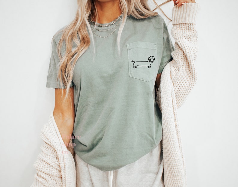 May include: A sage green t-shirt with a small black dachshund graphic on the pocket.