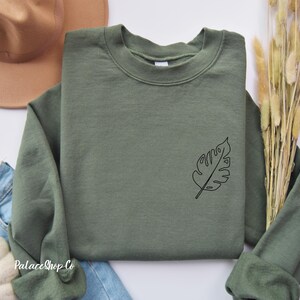 May include: A green sweatshirt with a simple line drawing of a leaf on the left side of the chest.