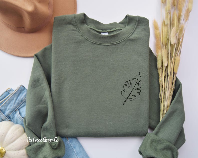 May include: A green sweatshirt with a simple line drawing of a leaf on the left side of the chest.