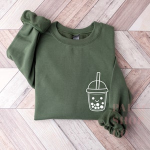 May include: A dark green sweatshirt with a white outline of a smiling boba tea cup with a straw.