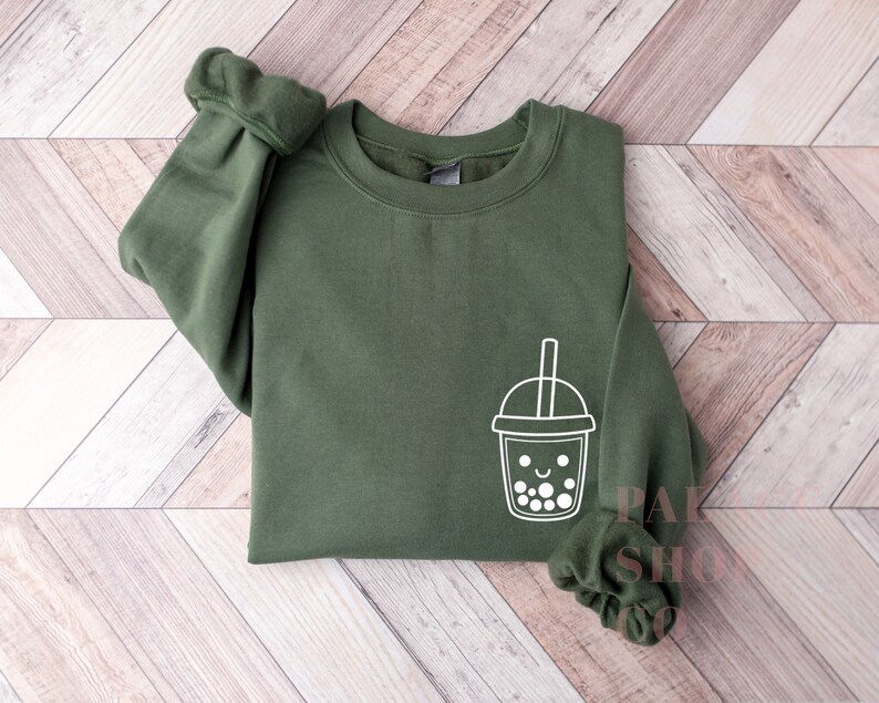 May include: A dark green sweatshirt with a white outline of a smiling boba tea cup with a straw.