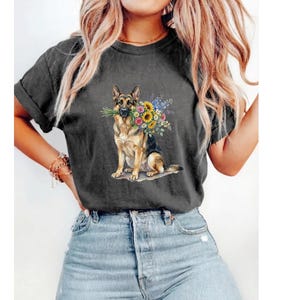 Peut inclure: T-shirt gris fonc&eacute; avec une illustration &agrave; l'aquarelle d'un berger allemand tenant un bouquet de tournesols et d'autres fleurs color&eacute;es. Le chien est assis et le t-shirt a des manches retrouss&eacute;es.