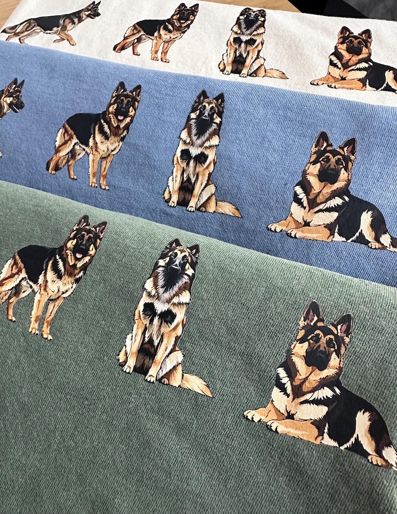 Op de afbeelding: Close-up van drie stoffen stalen in wit, blauw en groen, elk bedrukt met herhaalde illustraties van Duitse herders in verschillende poses. De honden zijn afgebeeld in zwart, bruin en bruin.