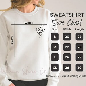 May include: White sweatshirt with a size chart showing measurements in inches. The chart includes sizes S, M, L, and XL with corresponding width and length measurements. The text "Gigi" is written on the sweatshirt with a heart.
