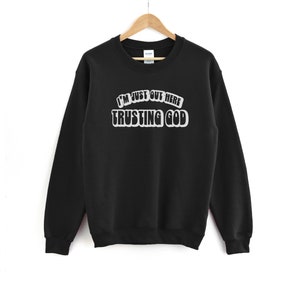 May include: Black sweatshirt with the text "I'm just out here trusting God" in white lettering.