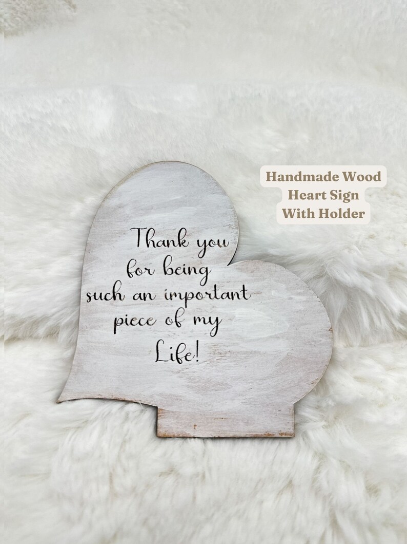 May include: A handmade wooden heart-shaped sign with a holder. The sign is painted white with distressed edges and features the text "Thank you for being such an important piece of my Life!" in black script.