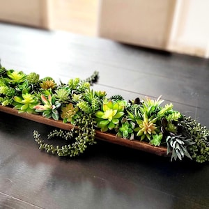 May include: A wooden trough filled with a variety of green succulents, arranged in a cascading design. The trough is sitting on a dark wood surface.