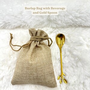 May include: A burlap bag with a gold spoon. The bag is tied with a string and the spoon has a leaf design. The text "Burlap Bag with Beverage and Gold Spoon" is written above the bag.