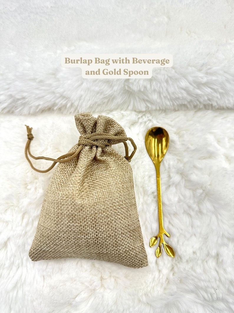 May include: A burlap bag with a gold spoon. The bag is tied with a string and the spoon has a leaf design. The text "Burlap Bag with Beverage and Gold Spoon" is written above the bag.