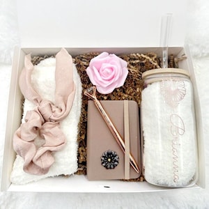 May include: A gift box filled with a white fuzzy headband, a pink rose, a brown notebook with a rose gold pen, and a clear glass tumbler with a straw and the name "Brianna" written on it.