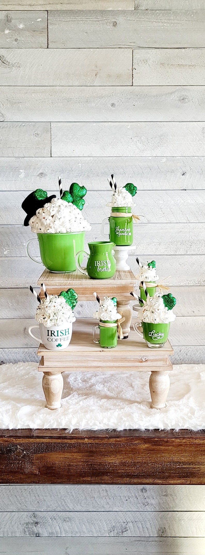 May include: A tiered wooden stand with four green and white mugs with whipped cream and shamrock decorations. The mugs are labeled "Irish Coffee", "Irish Creme", "Shamrock Sweet", and "Lucky".