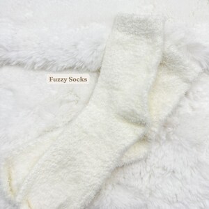 May include: A pair of white fluffy socks on a white fluffy surface. The socks are folded in half and the text "Fuzzy Socks" is visible in the image.
