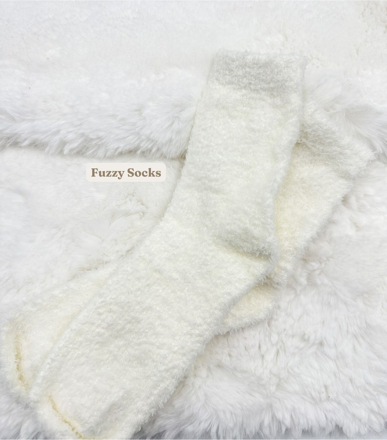 May include: A pair of white fluffy socks on a white fluffy surface. The socks are folded in half and the text "Fuzzy Socks" is visible in the image.