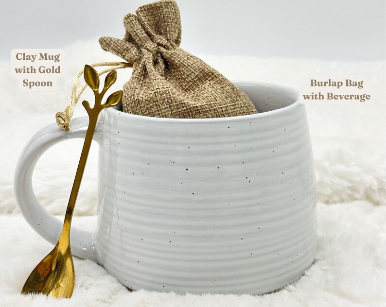 May include: A white clay mug with a gold spoon and a burlap bag inside. The mug has a handle and a textured, ridged design. The gold spoon has a leaf-like design at the top. The burlap bag is tied with a string.