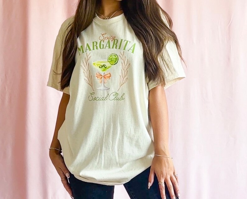 May include: A beige t-shirt with a graphic of a margarita glass with a lime wedge and the text "Spicy Margarita Social Club".